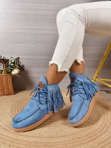 Detail van blauwe suède enkellaarzen met franjes in westernstijl en studs.