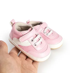 Close-up of pink and white baby canvas sneakers held in hand showing soft material.