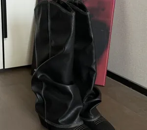 Detailed view of fashionable black slouchy high-tube leather boots with contrast stitching