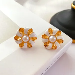 Gros plan de boucles d'oreilles fleurs vintage en émail blanc avec centre en perle