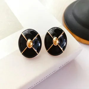 Detailed macro shot of vintage black enamel stud earrings with elegant gold cross pattern