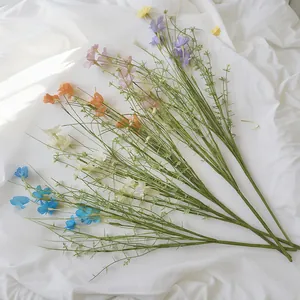 Detailansicht bunter künstlicher Wildblumen mit langen grünen Stielen auf weißem Stoff