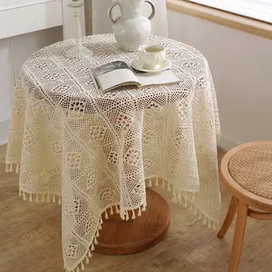 Detalle de un mantel de ganchillo crema con borlas en un entorno de habitación rural