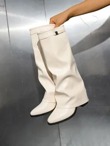 Detail van gebroken witte laarzen met plooien, decoratieve riem en puntige neus