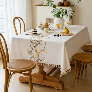 Close-up detail of yellow floral embroidery and fringe tassels on a cream linen tablecloth