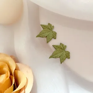 Macro di orecchini a lobo a forma di foglia verde con trame realistiche su seta bianca