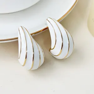 Detailaufnahme von weißen Emaille-Ohrringen in Tropfenform mit goldfarbenen Streifen.