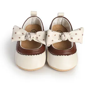 Close-up of cream baby princess shoes with a large polka-dot bow and brown trim