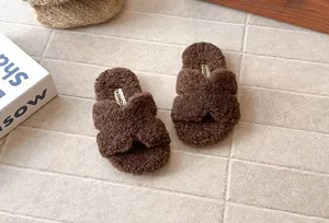 Dettaglio di ciabatte in peluche marrone con cinturino a incrocio per bambini a terra