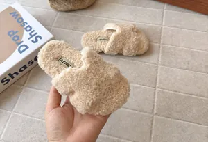 Primo piano della morbida consistenza sherpa beige delle pantofole di peluche per bambini.