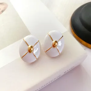 Detail view of vintage white enamel stud earrings with gold-tone cross design accents.