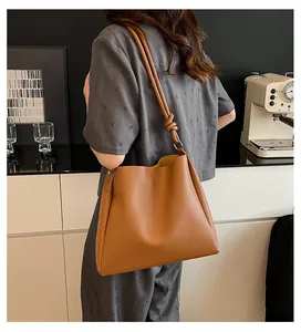 Model wearing a large camel brown faux leather tote bag with knotted shoulder strap.