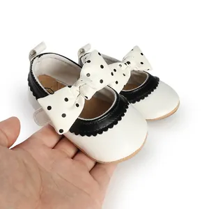 Close-up of white baby princess shoes with black polka dot bows and scalloped trim