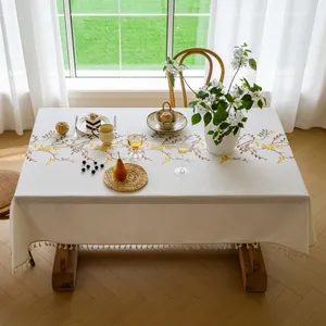 Detailed view of an elegant linen tablecloth with yellow floral embroidery and fringe