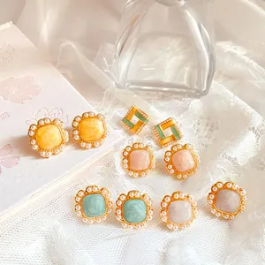 Close-up of French vintage enamel stud earrings with elegant pearl borders and warm pastel tones