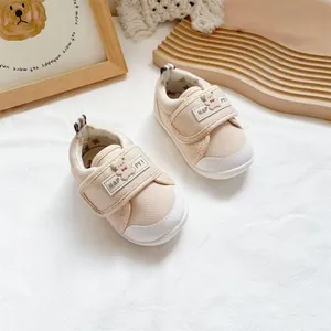 Close-up detail of beige baby walking shoes with cartoon bear and velcro strap.