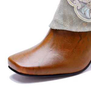 Close-up detail of square toe burnished leather boot with ethnic embroidery and denim