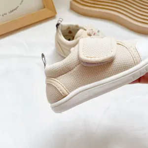 Side detail view of beige breathable fabric baby walking shoes with soft sole and velcro strap.