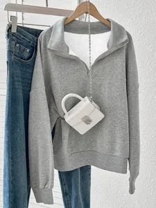 Detail einer grauen Sweatshirt-Jacke kombiniert mit einer kleinen weißen Kroko-Handtasche