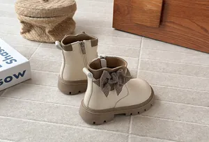 Detail view of cream girls' leather boots with a houndstooth bow and thick sole.