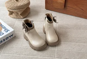 Close-up detail of kids beige leather ankle boots with houndstooth bow and side zipper