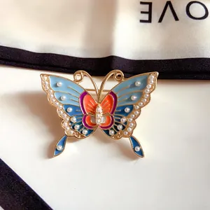 Close-up of a vintage enamel butterfly brooch with pearl embellishments on silk.