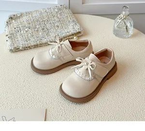 Detail view of cream girls' leather loafers featuring elegant bow and lace trim