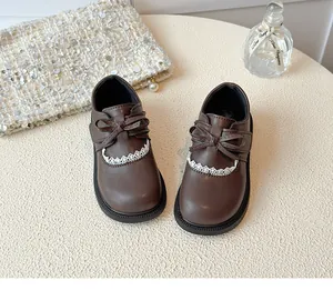 Close-up of girl's brown leather shoes featuring lace trim and bow details on top.