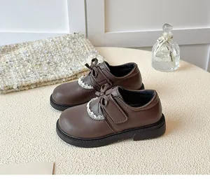 Close-up detail of dark brown children's leather shoes with elegant bow and lace trim