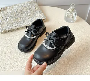 Close-up of girls' black Mary Jane shoes with bow and lace detail on a soft sole.