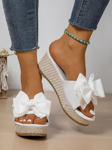 Detail view of stylish white wedge sandals featuring a large decorative bow on the strap.