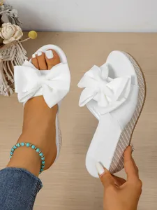 Detail view of women's white wedge sandals with oversized bow and woven sole