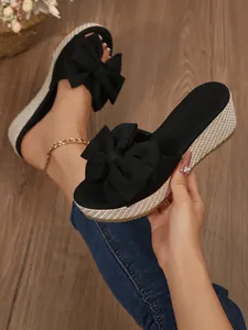 Detailed shot of black wedge sandals featuring a large bow and a stylish woven platform sole.