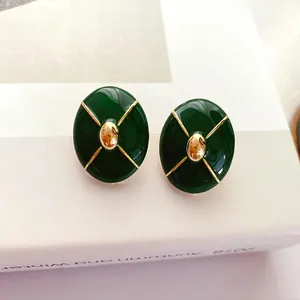 Macro shot of vintage dark green enamel stud earrings with gold cross pattern details.