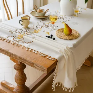 Close-up detail of a beige tablecloth featuring elegant floral embroidery and tassel edges