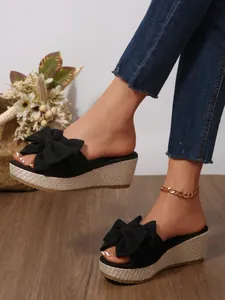 Detailed view of black wedge sandals featuring a large bow knot and woven platform sole