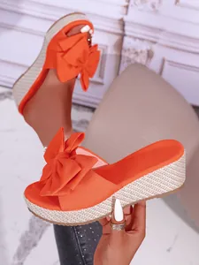 Close-up of orange wedge sandals featuring large bow design and woven platform