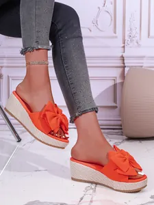 Detailed view of bright orange wedge slippers with a large bow and woven sole