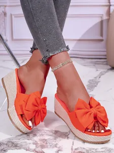 Detail view of bright orange wedge sandals featuring a large bow and braided sole