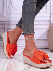 Close-up detail of stylish orange bow wedge slippers with textured straw platform sole