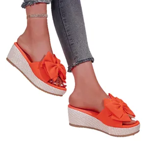 Stylish women's orange wedge slippers featuring a large bow and woven platform sole