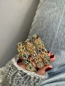 Macro view of three golden C-shaped bracelets with colorful evil eye and gemstone patterns
