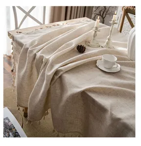 Close-up detail of a natural linen tablecloth with elegant tassel edges on a wooden table