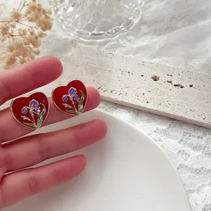Primo piano di orecchini vintage a cuore in smalto con motivo floreale di iris in mano.