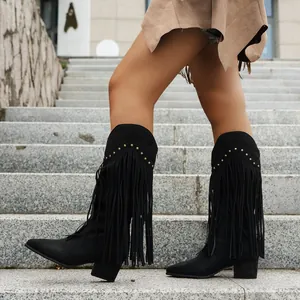Stylish black suede Western fringe boots with metal studs on grey stone steps.