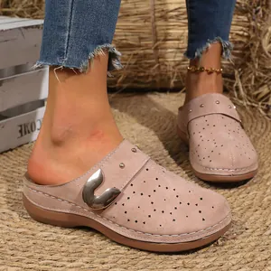 Close-up of pink suede clogs with floral cutouts and metal buckle on rustic mat
