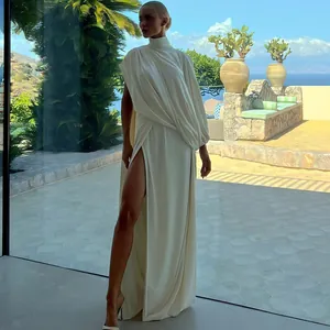 Elegant white high-neck pleated top and high-slit skirt set against a scenic sea backdrop.