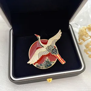 Primer plano de un elegante broche vintage de esmalte de grulla con sol rojo en caja