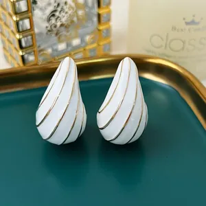Detaillierte Makroansicht weißer Emaille-Ohrhänger mit eleganten goldenen Spirallinien