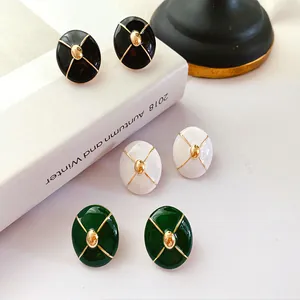 Close-up of vintage enamel stud earrings with gold cross pattern and silver needles.